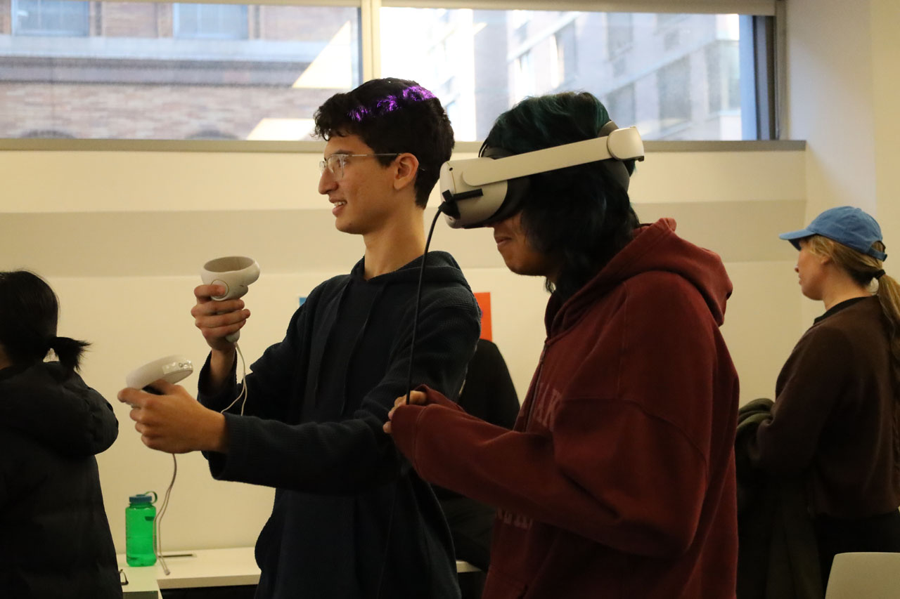 Two students play with a VR headset. One is wearing the headset while the other uses the controllers.