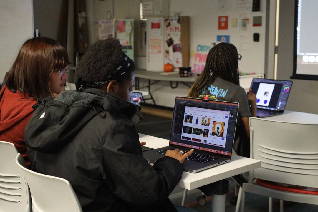 A student posing with a snowman figurine in front of a green screen while another student takes her photo.