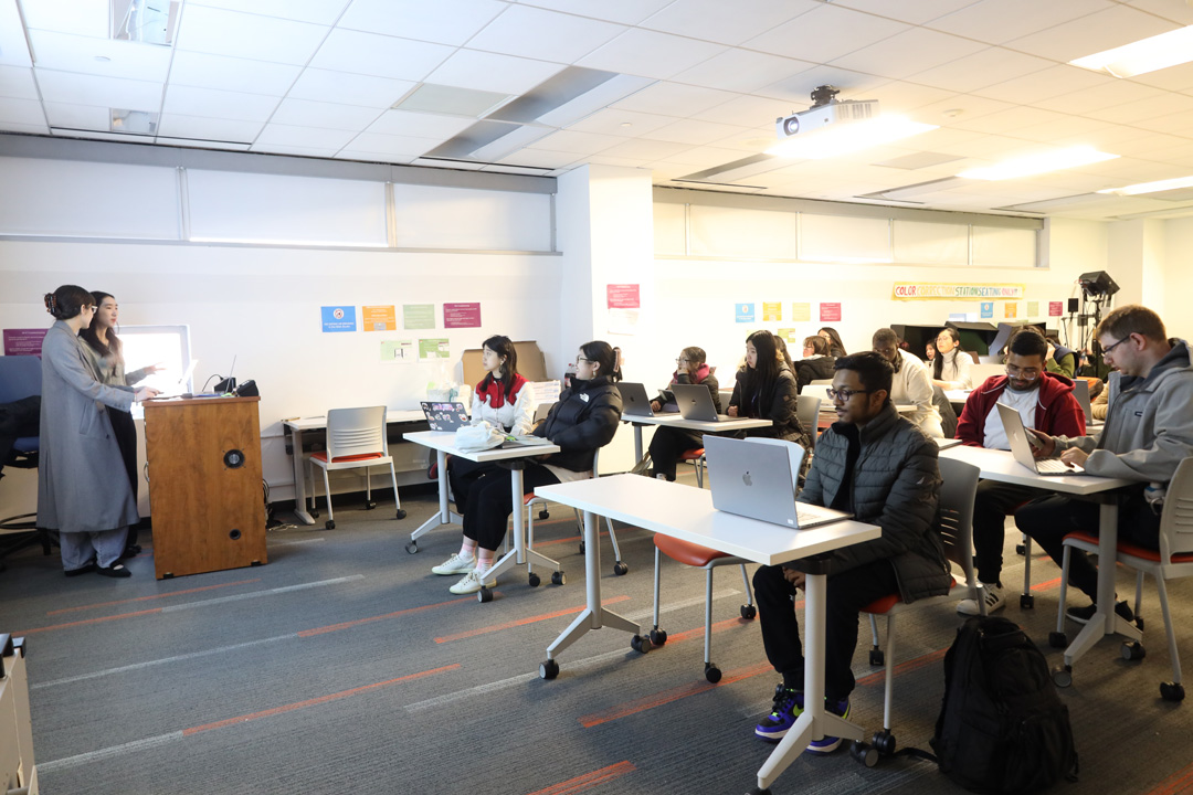 Students sitting at tables in the NMA Studio with two docents at a podium in the front of the room.