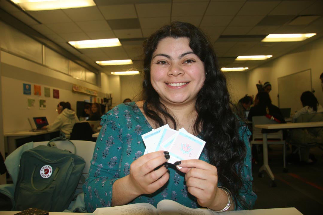 Woman with dark long hair smiling and holding up a couple square stickers.