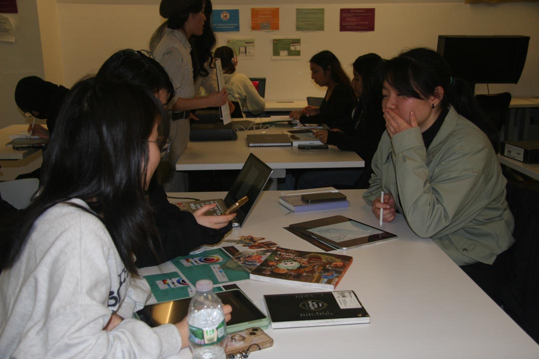 Three students sitting around a desk with tablets and a laptop.
