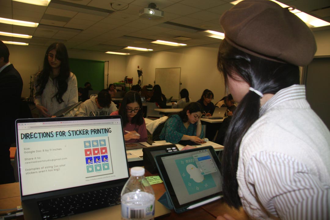 Back view of a person with a side ponytail standing in front of a classroom. A laptop in front of them shows a presentation on sticker printing.