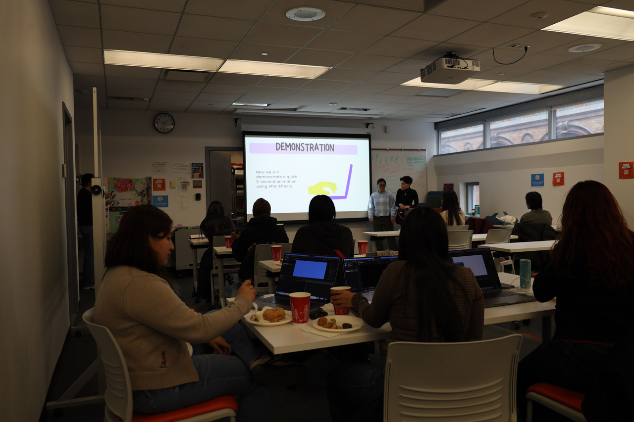 Students sitting at tables in the NMA Studio with a docent at a podium in the front of the room. The projector screen says 'Demonstration'.