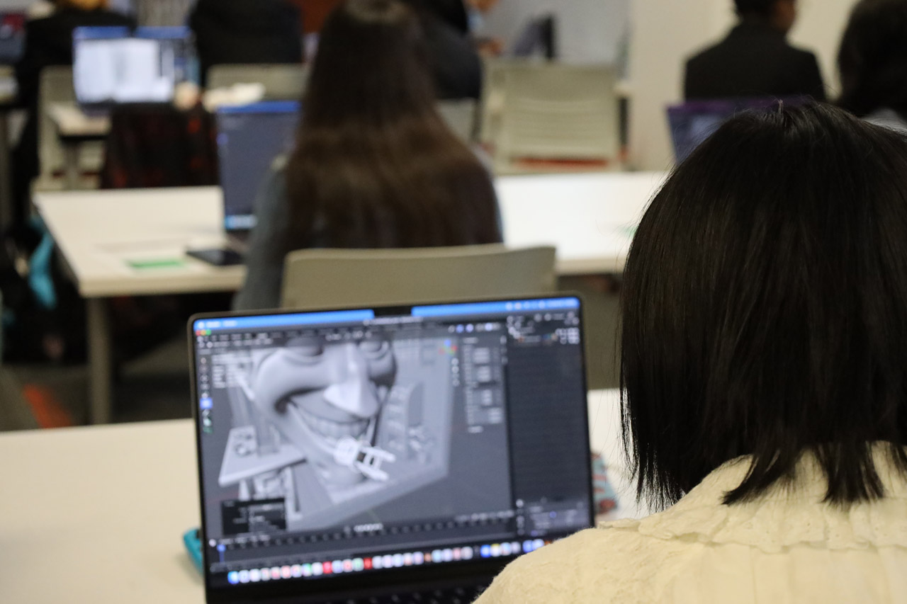 A student works on a model of a large face in a small room in Blender.