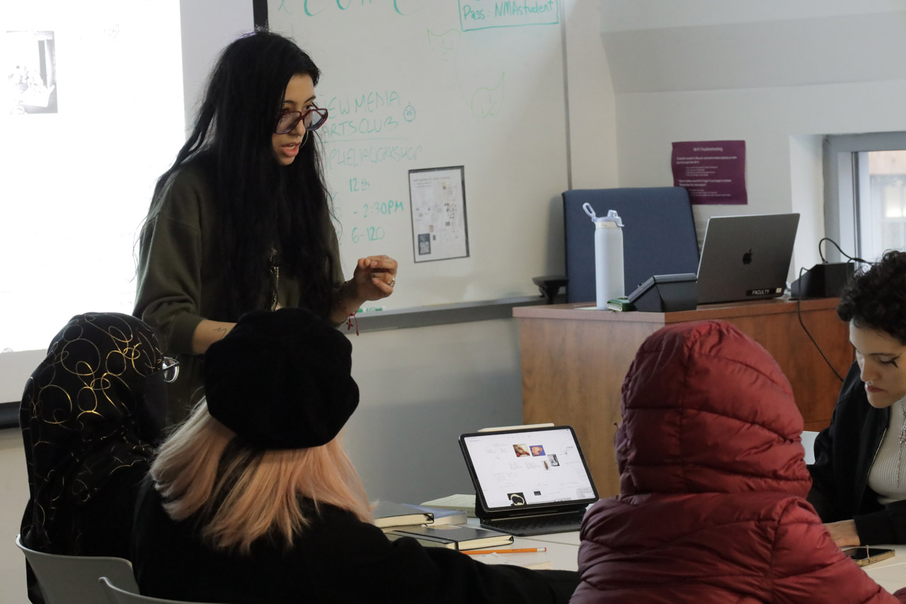 A woman with long black hair shows students a mindmap on her iPad.